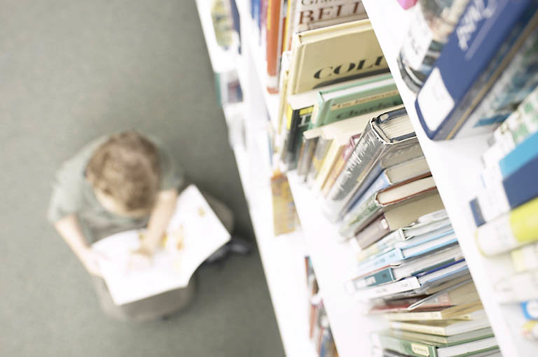 Little boy reading book beside library shelf 2