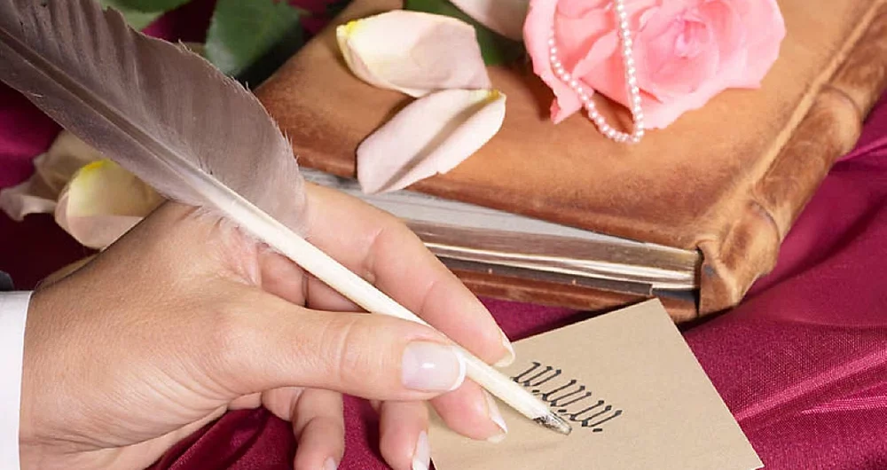 Woman writing web address with quill next to old leather book and rose